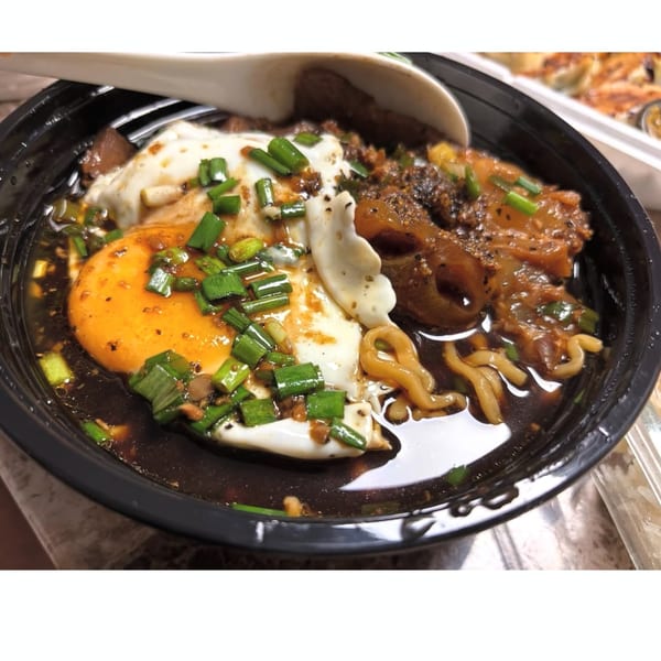 Taiwanese noodle soup with a fried egg, green onions, and braised pork in a black bowl.