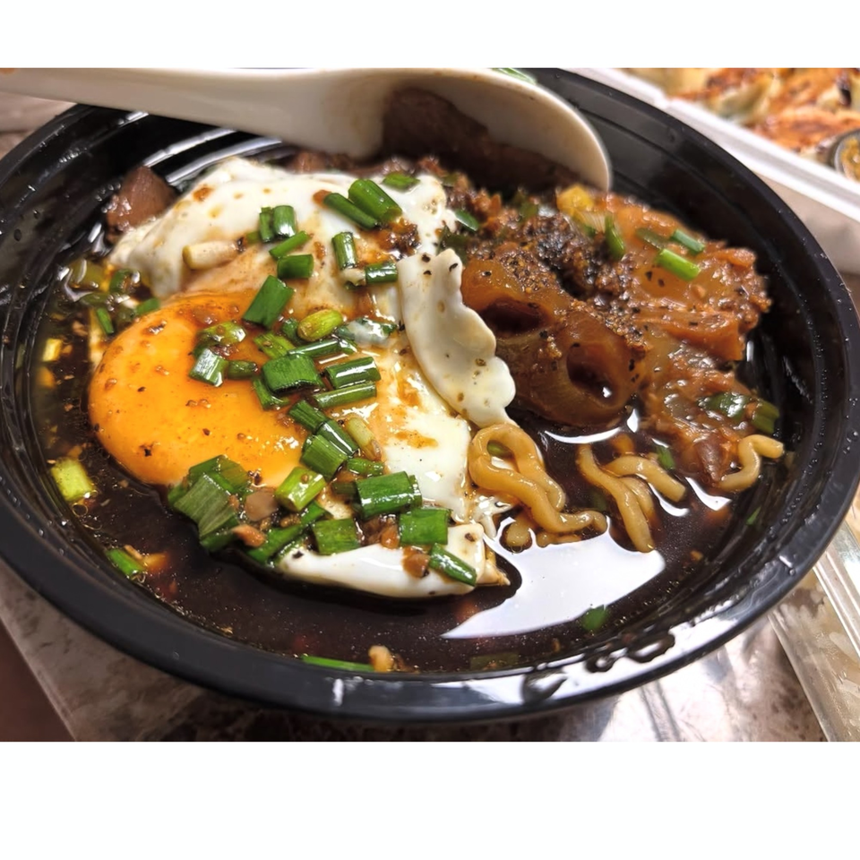 Taiwanese noodle soup with a fried egg, green onions, and braised pork in a black bowl.